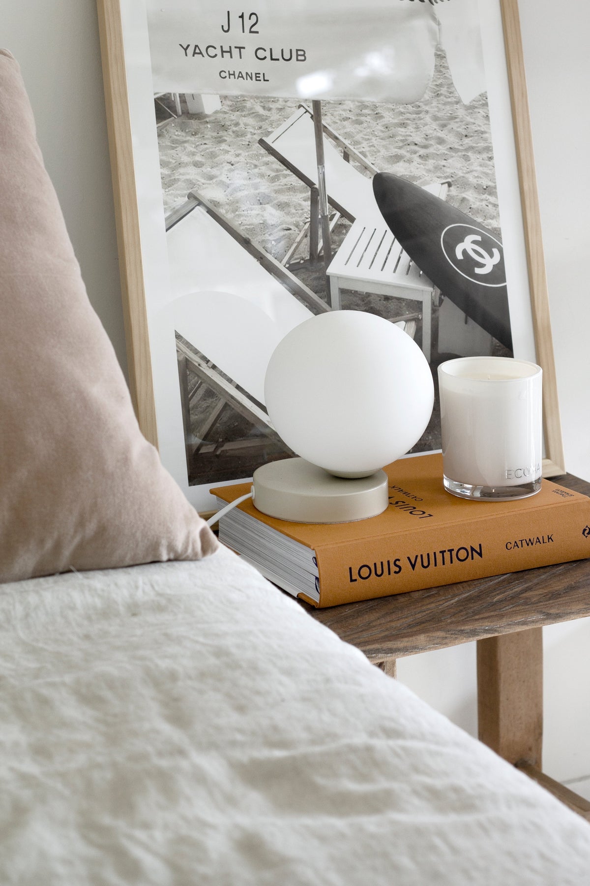 Bedside table with a globe lamp, a candle and a Louis Vuitton book beneath a framed print