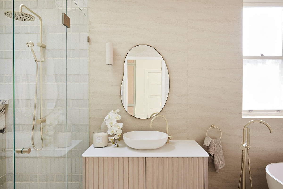 House 17 by Three Birds Renovations: bathroom with a fluted timber vanity, round vessel basin, organic mirror, brushed brass tapware and a walk-in shower