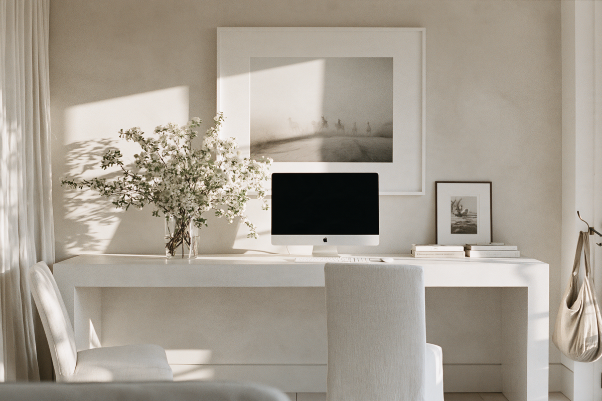 White desk with a computer, framed black and white print and a glass vase of flowering branches