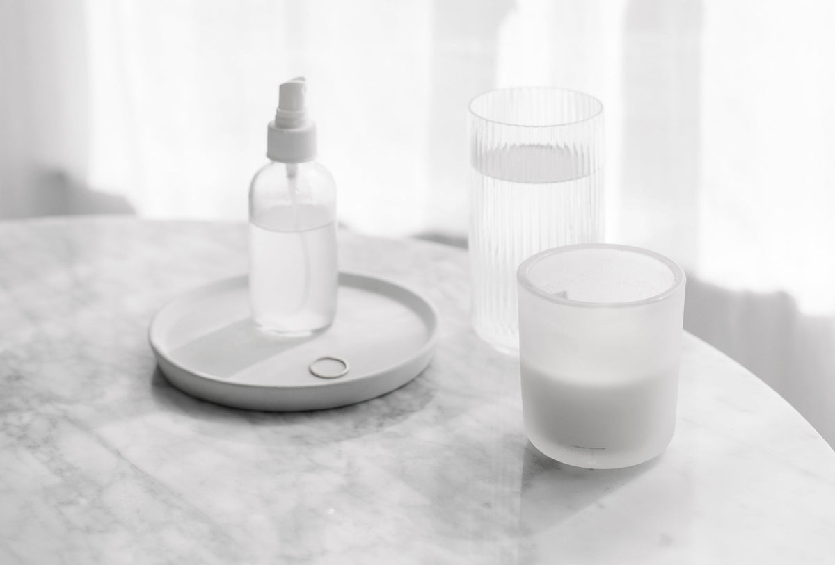 Spray bottle on a round tray beside glasses of water on a marble table
