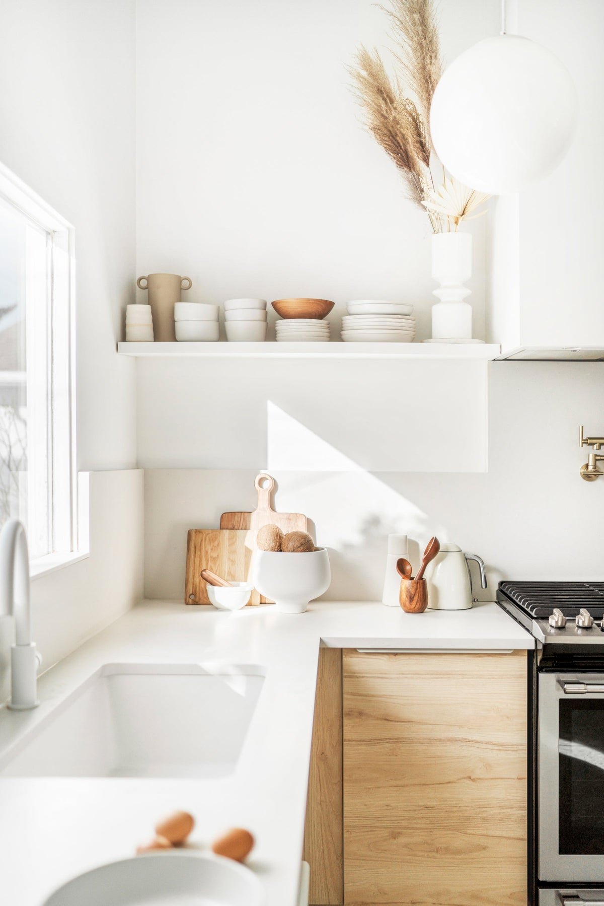 Bright kitchen with open shelves of ceramics, a timber cabinet and a vase of dried grasses