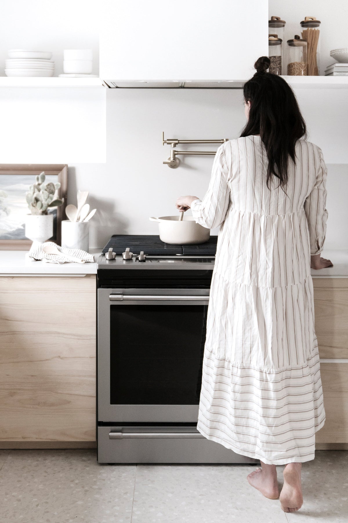 Woman in a striped dress cooking at a stove in a pale timber kitchen