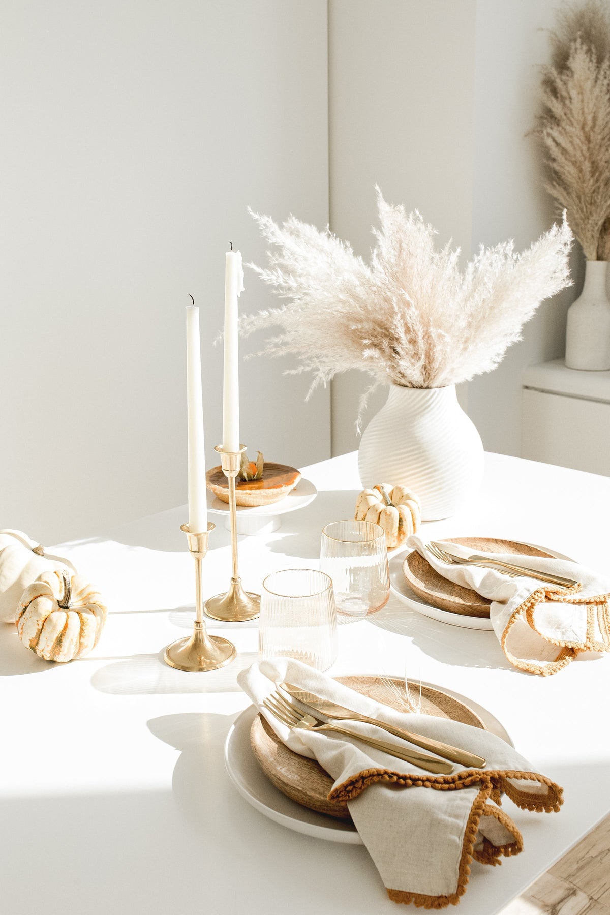 Table set with gold cutlery, linen napkins, taper candles and a vase of dried grasses