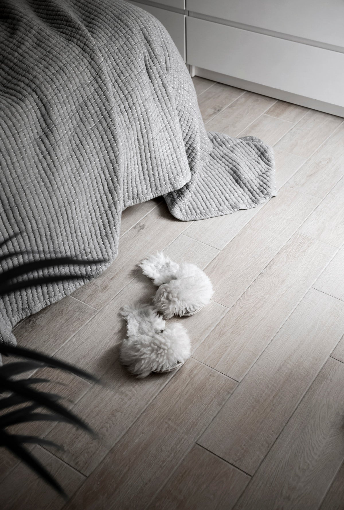 Knit throw spilling from a bed onto timber floorboards beside fluffy slippers