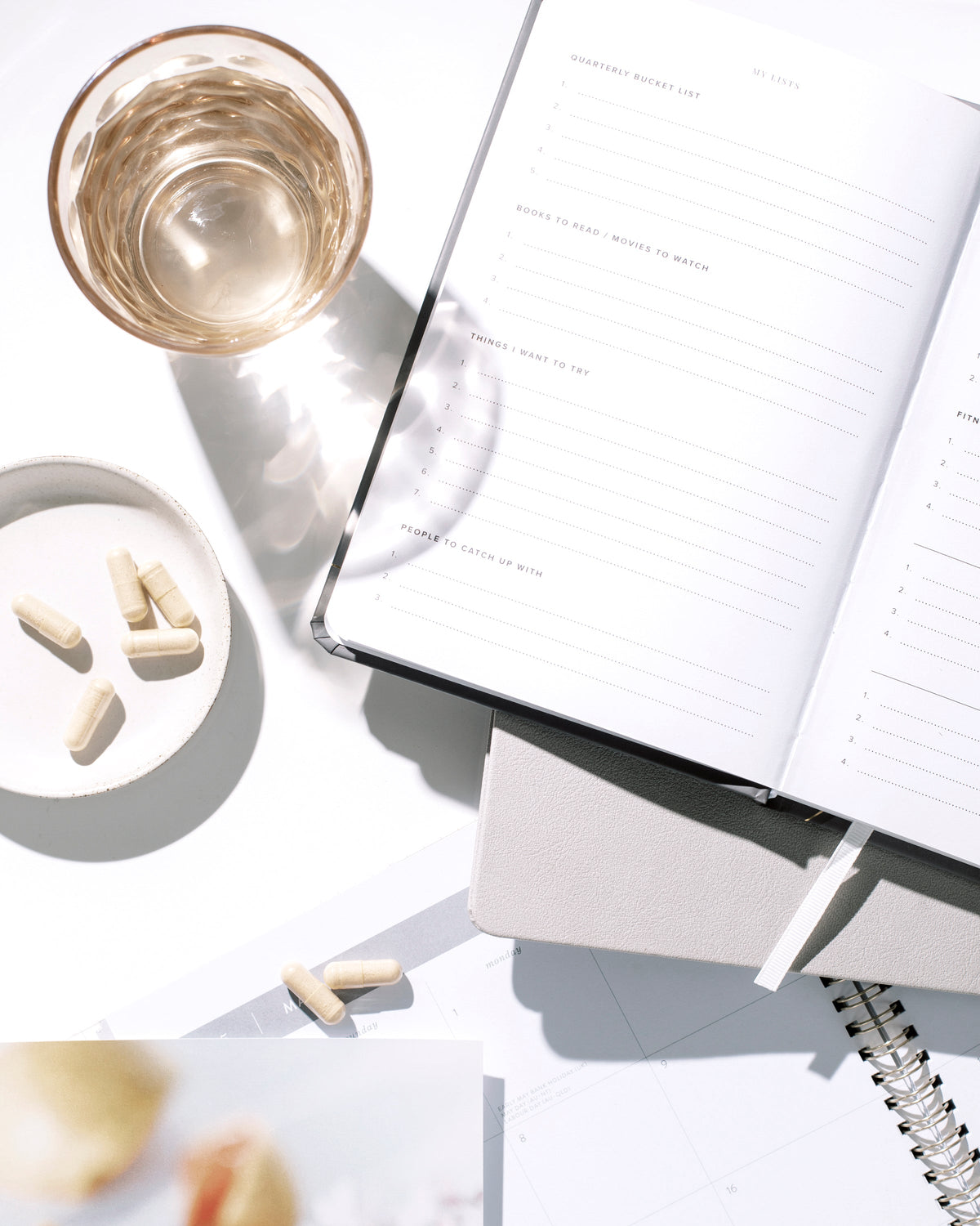 Open planner beside a glass of water and a small dish on a white desk