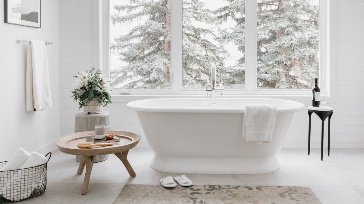 White bathroom with a freestanding bath, natural light, timber accents, candles, flowers and soft towels