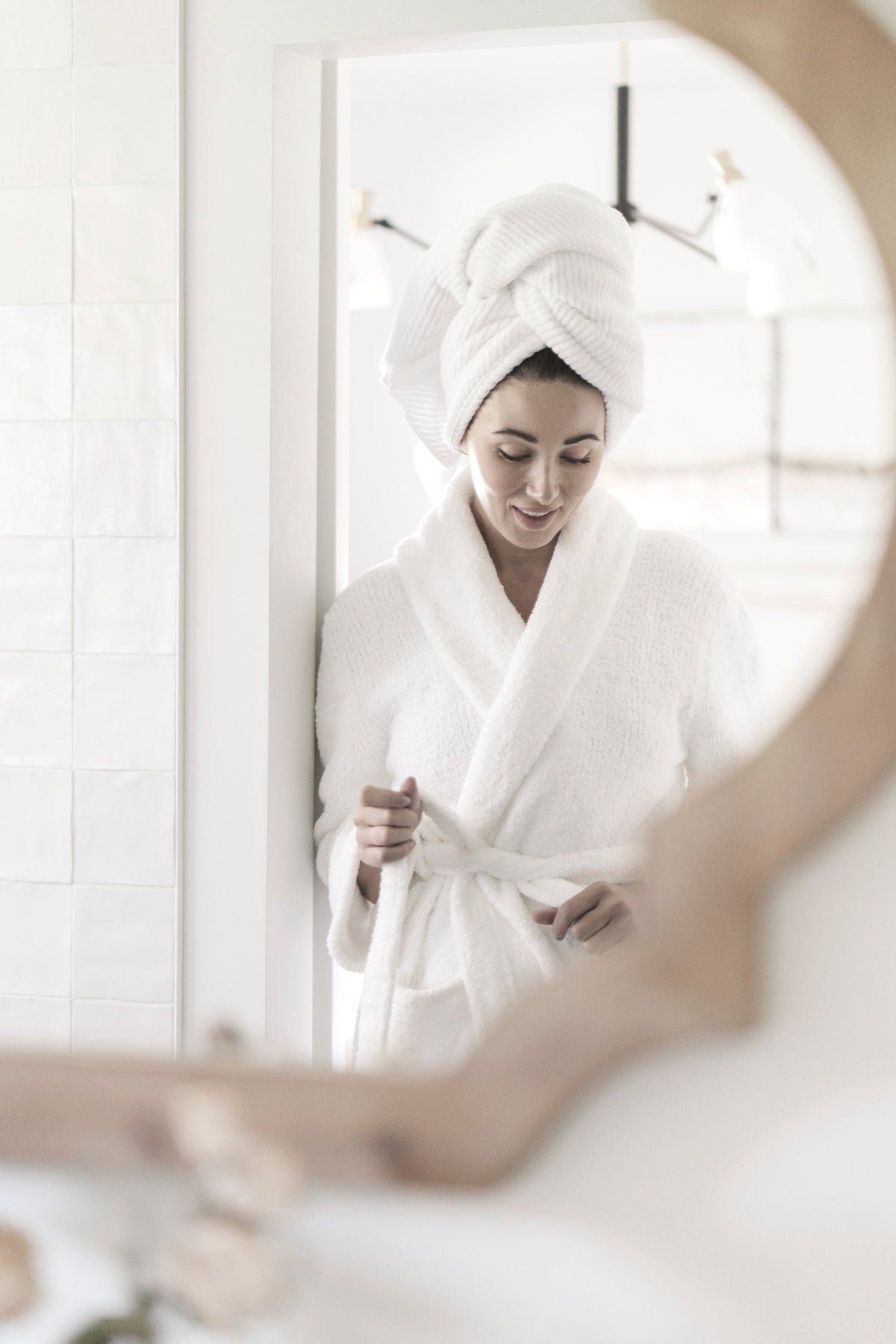 Woman in a white robe and towel turban reflected in a round mirror