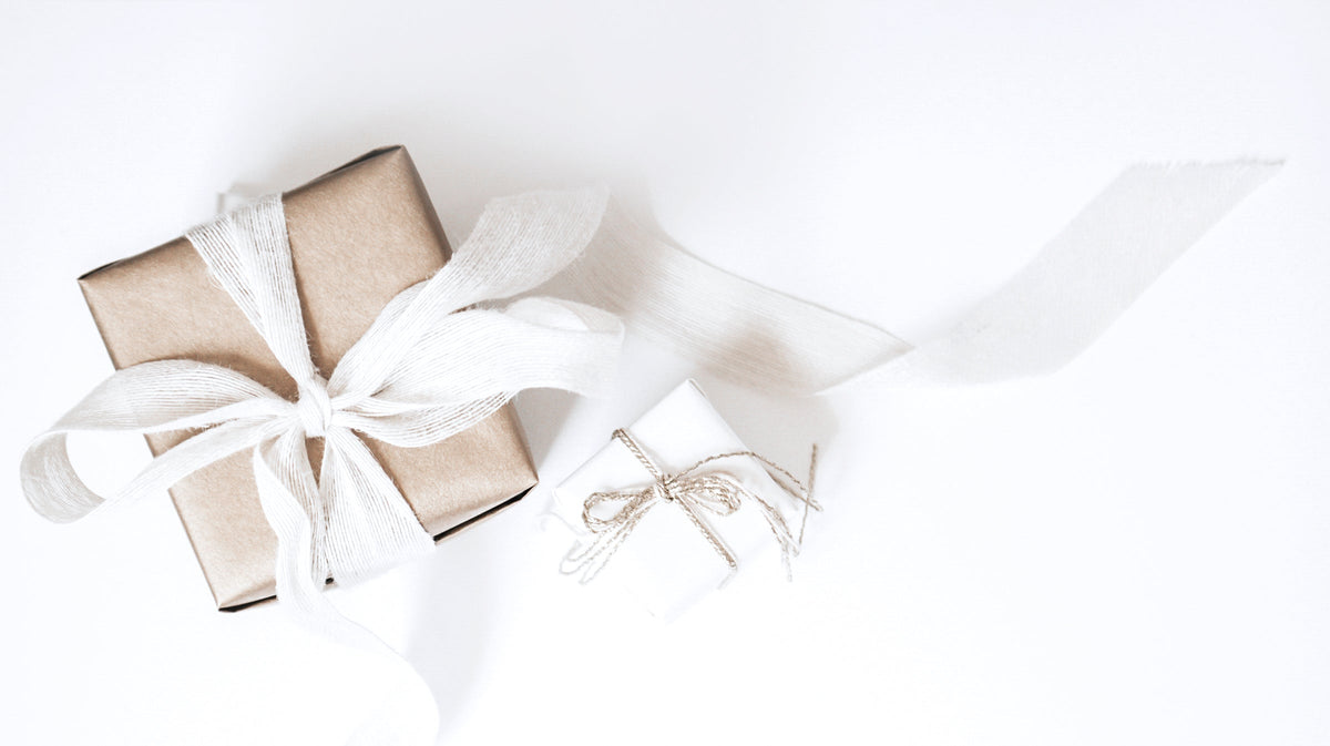 Two wrapped gifts, one in kraft paper with a white ribbon and one in white paper with twine, on a white background