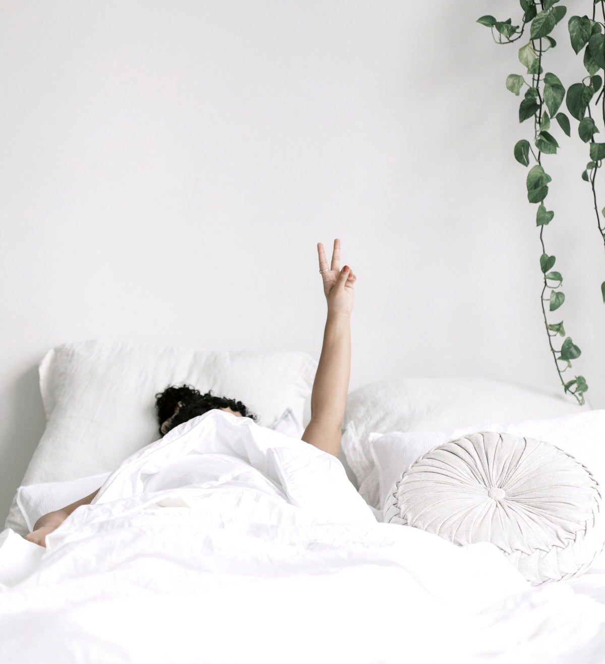 Person under white bedding with one hand raised in a peace sign