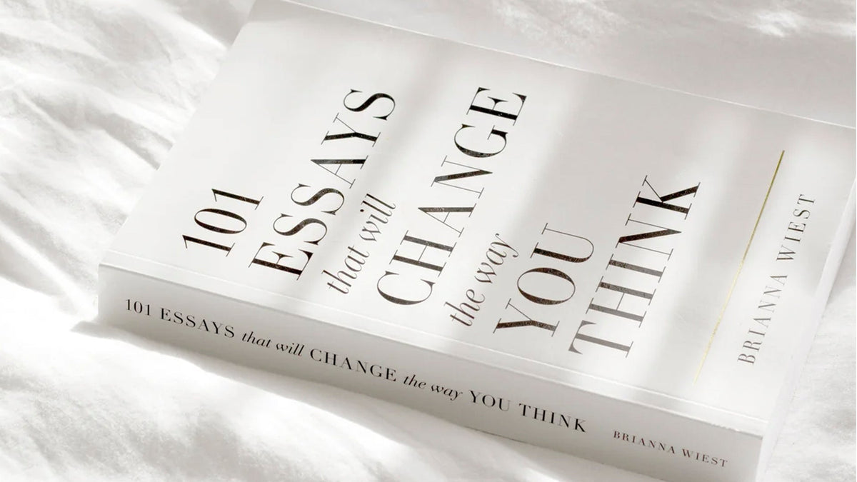Flatlay of the book “101 Essays That Will Change the Way You Think” by Brianna Wiest, resting on soft white bedding in natural light—evoking calm, clarity, and introspection.