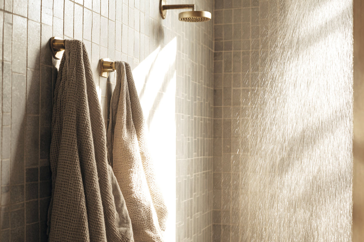 Linen towels hanging on hooks beside a tiled shower in soft evening light