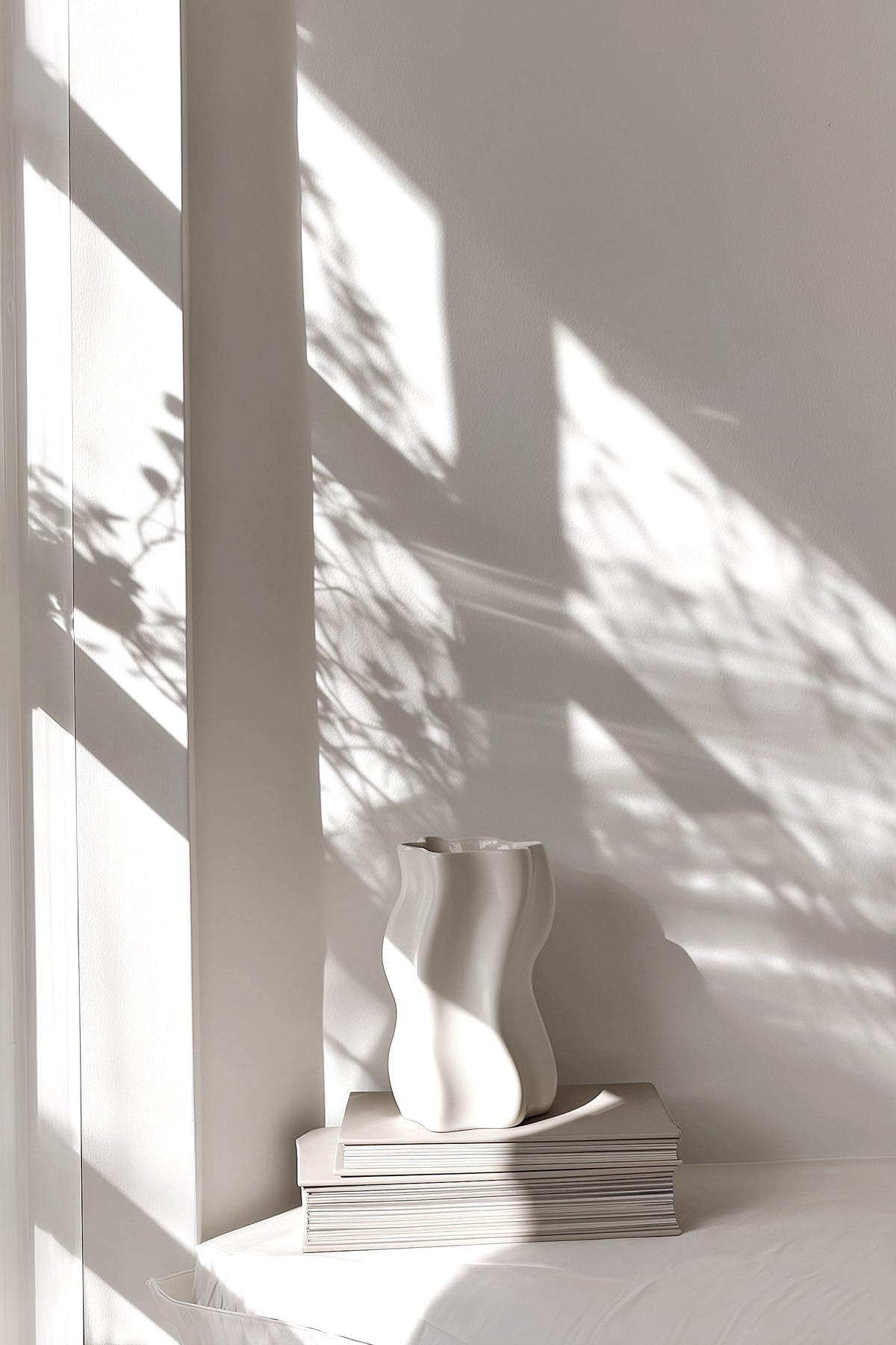 Sculptural vase on a stack of books in a corner patterned with leaf shadows