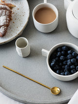 A tray with a cup of coffee and a bowl of blueberries, all beautifully arranged on a Zakkia Muddling Spoon - Brass / Silver.