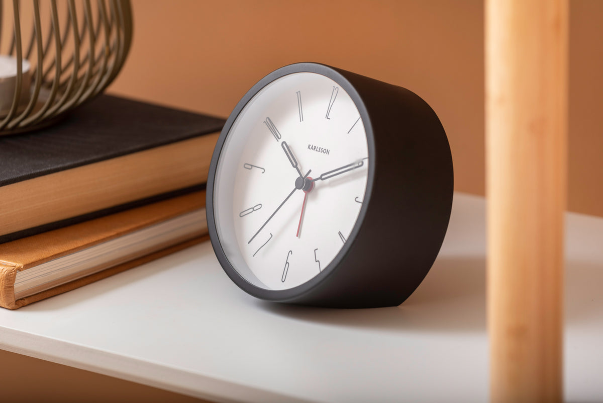 Black Belle alarm clock on a white shelf with books against a terracotta wall