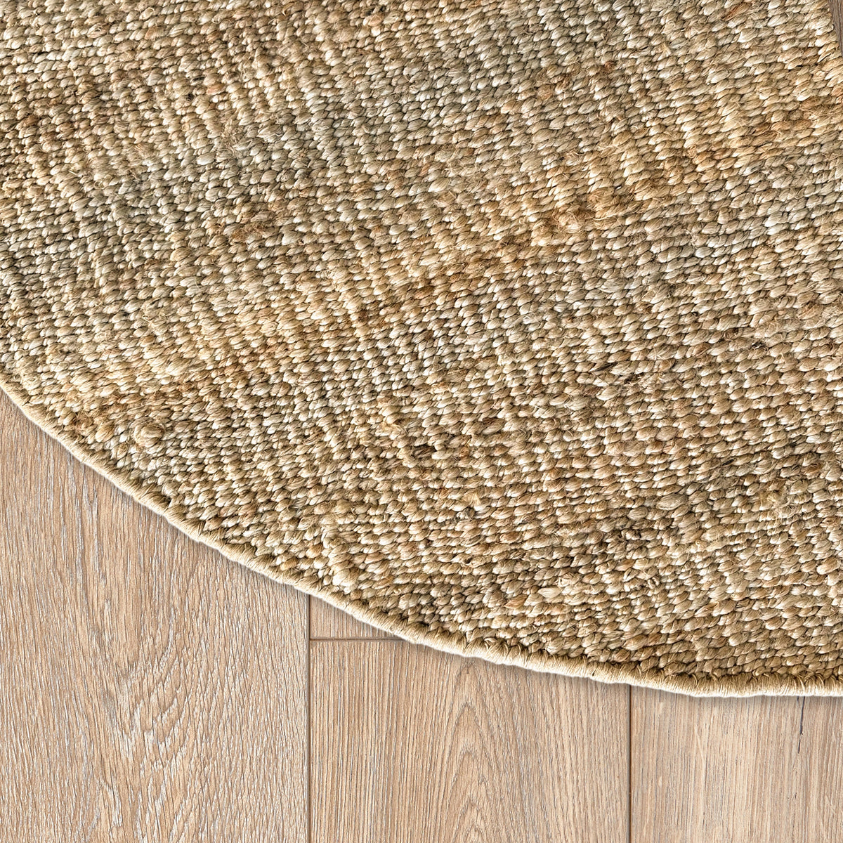 Curved edge of the round jute rug on a light oak floor