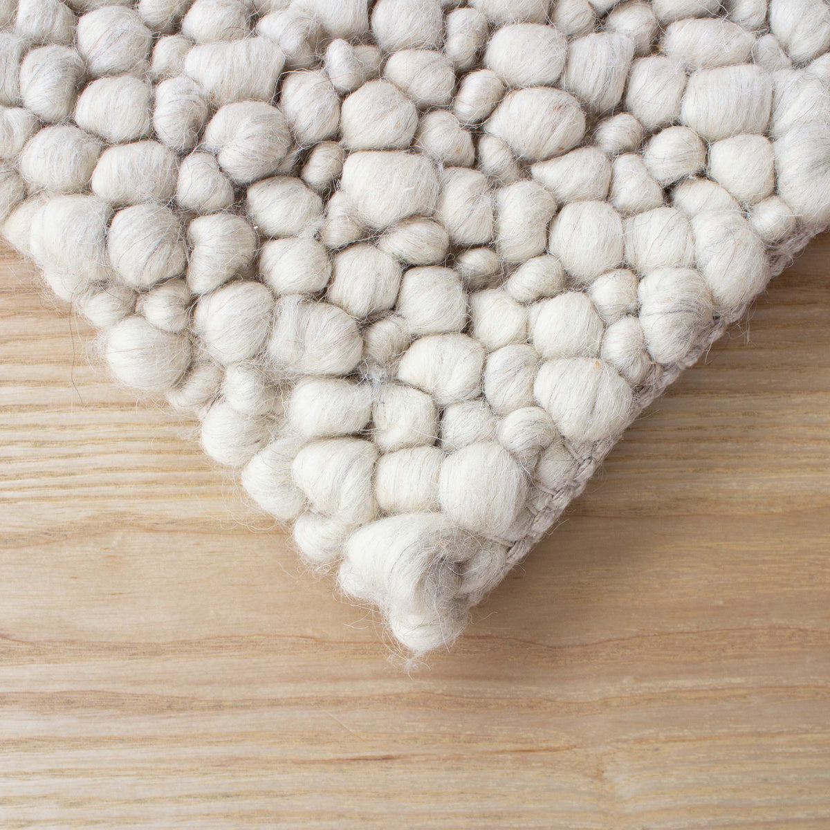 Corner of the beige pebble rug resting on a timber floor
