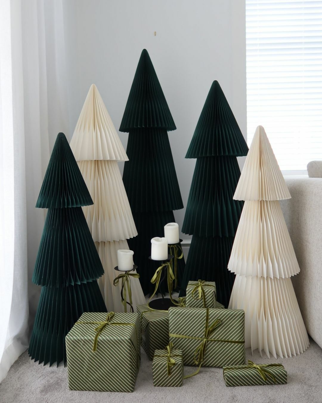 Beige paper Christmas trees grouped with dark green trees and wrapped gifts by a window