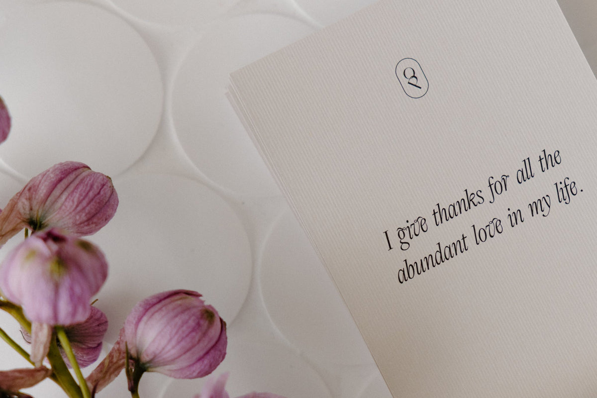 Affirmation card beside purple blooms on white linen