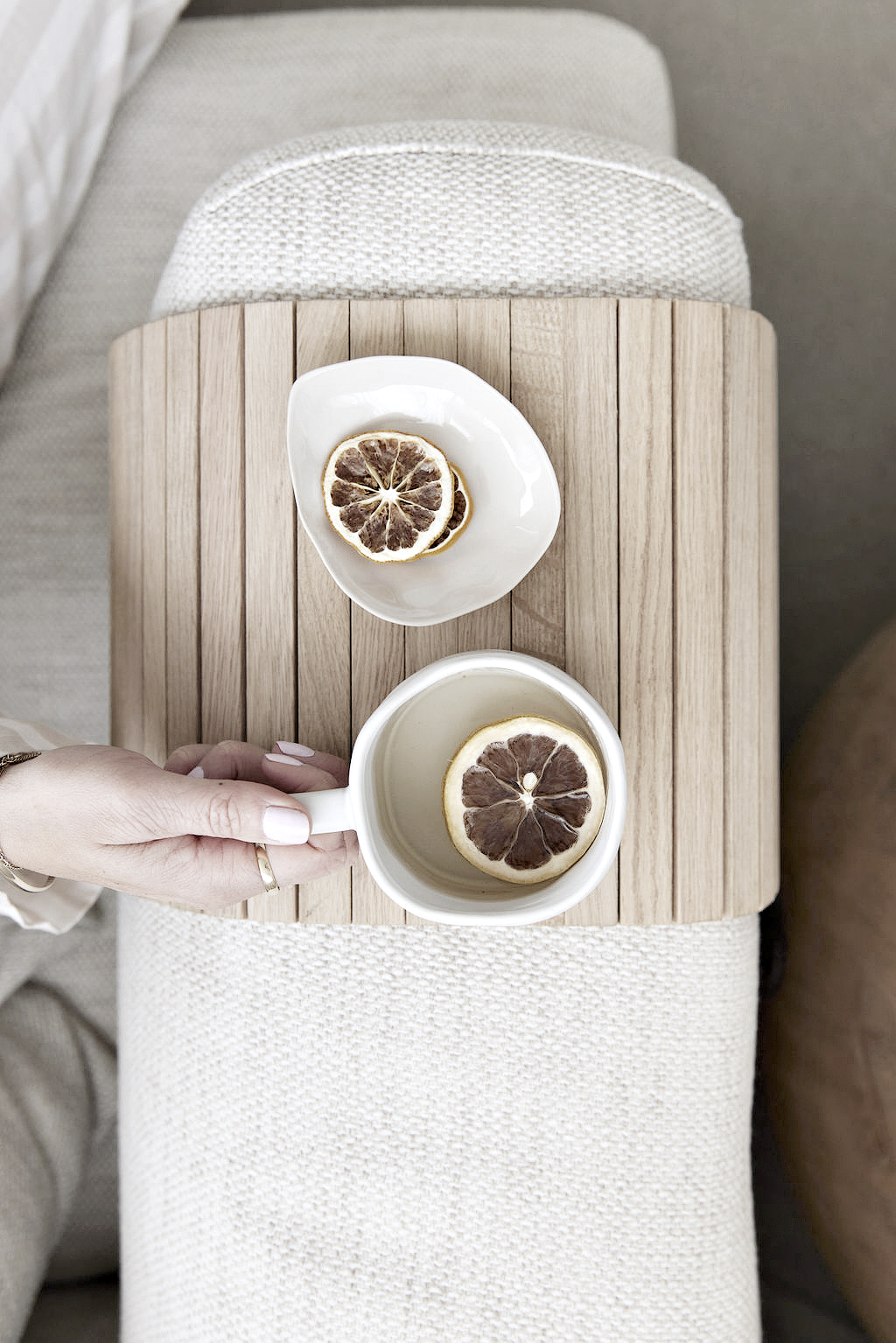 Oak slatted armchair tray over a sofa arm holding a mug and a small plate, each with a slice of dried lemon
