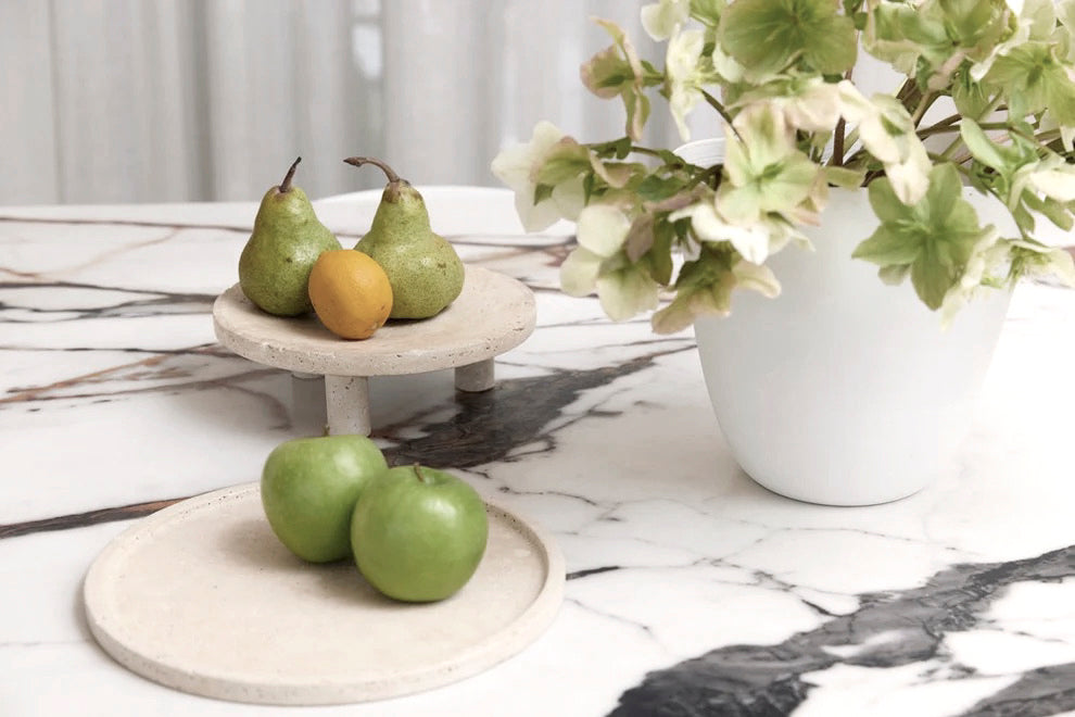 Light Travertine Nome stands holding pears and green apples on a marble table beside a potted plant