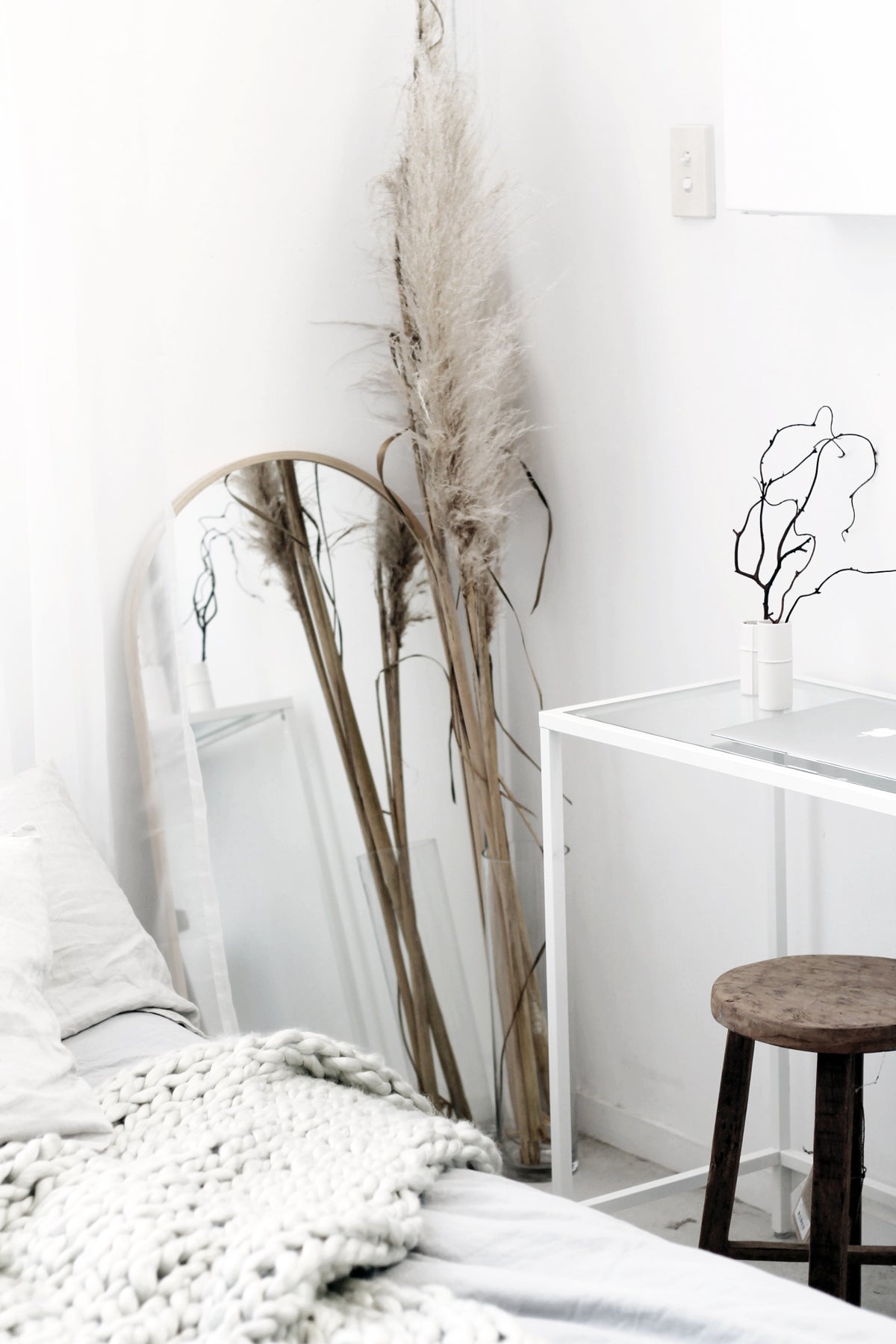 Dark-stained round stool beside a bed with pampas grass and a leaning mirror