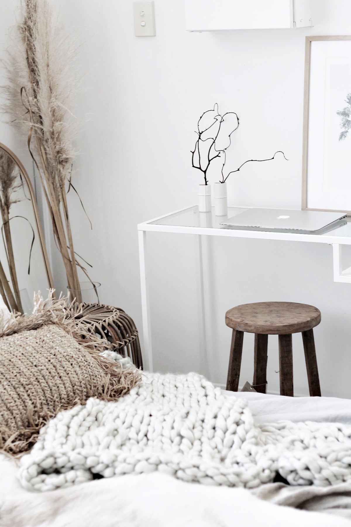 Dark-stained round stool beside a bed layered with a chunky knitted throw