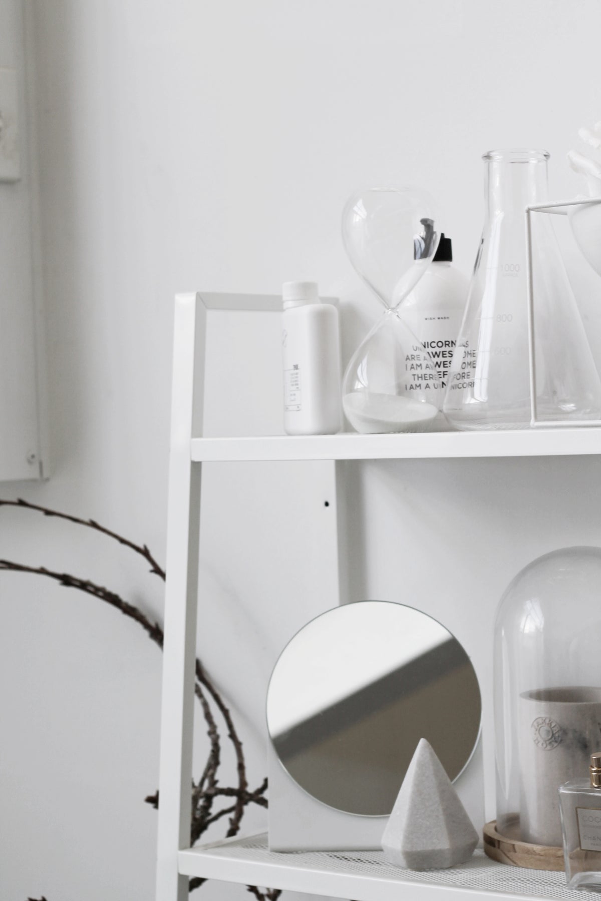 Hourglass on a white ladder shelf beside glass flasks, a bottle and a jar in soft light