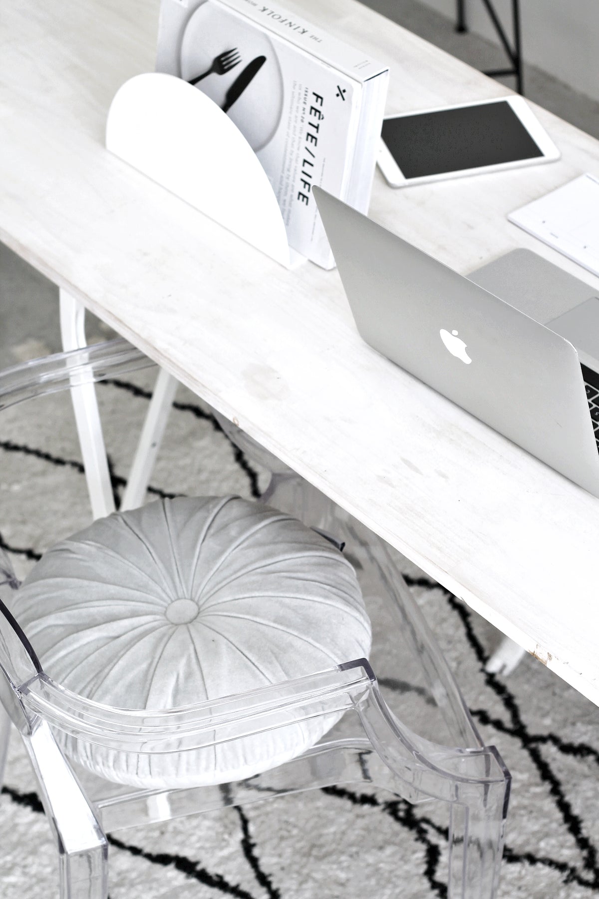 Clear acrylic armchair with a round tufted cushion at a pale timber desk with a laptop and tablet