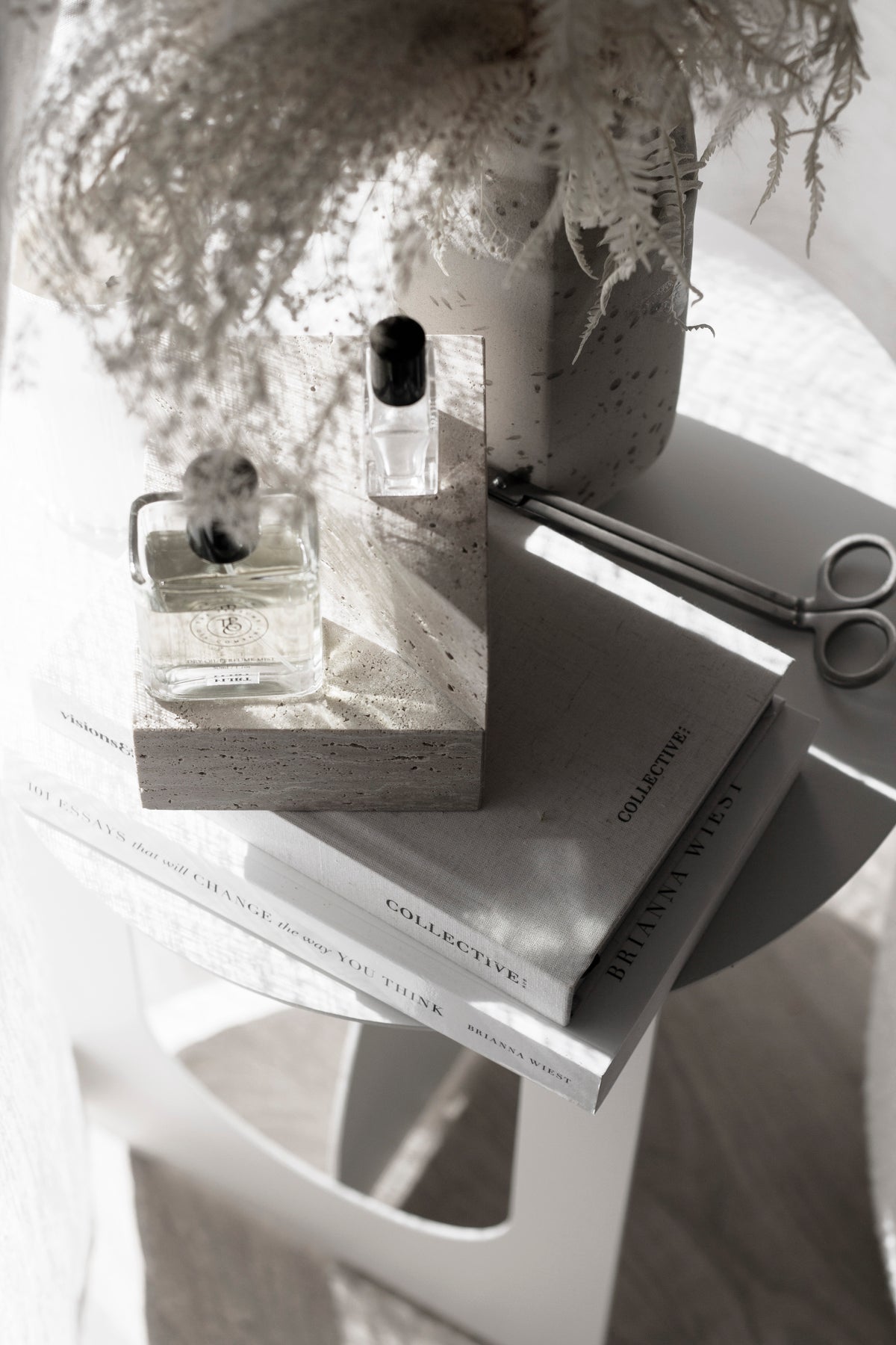 Travertine bookend used as a plinth for perfume bottles on a stack of books, with scissors and dried foliage alongside