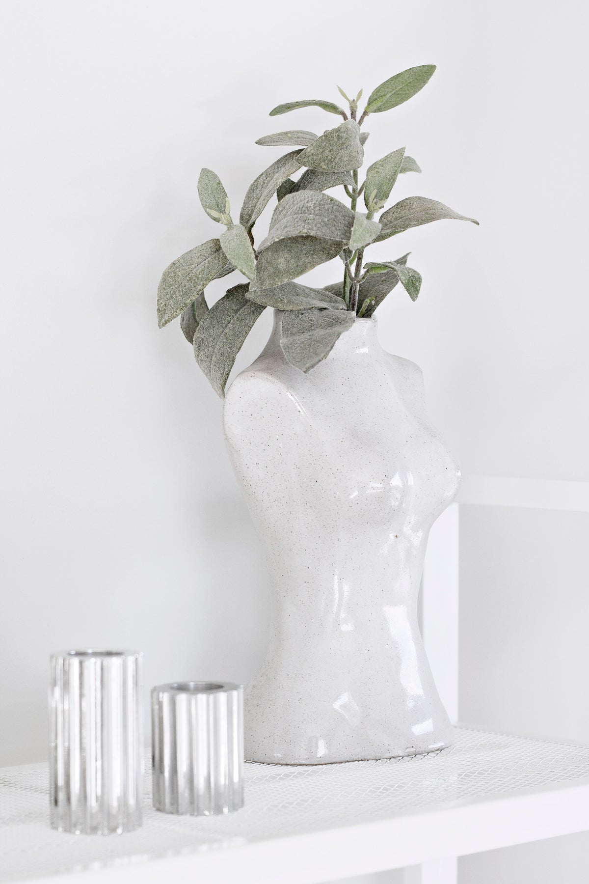 Close-up of the Female Silhouette Vase with sage foliage beside two ribbed glasses