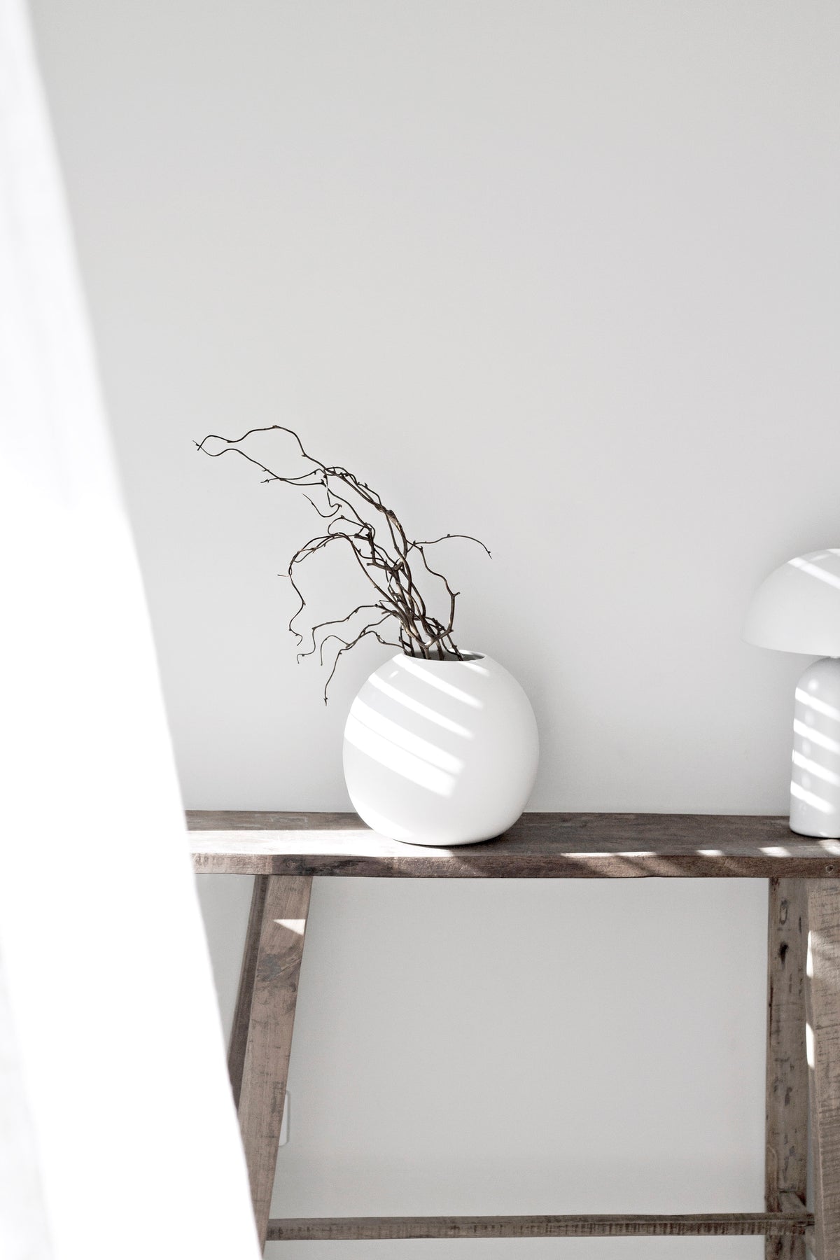 Recycled teak console against a white wall with a round white vase of twisted twigs