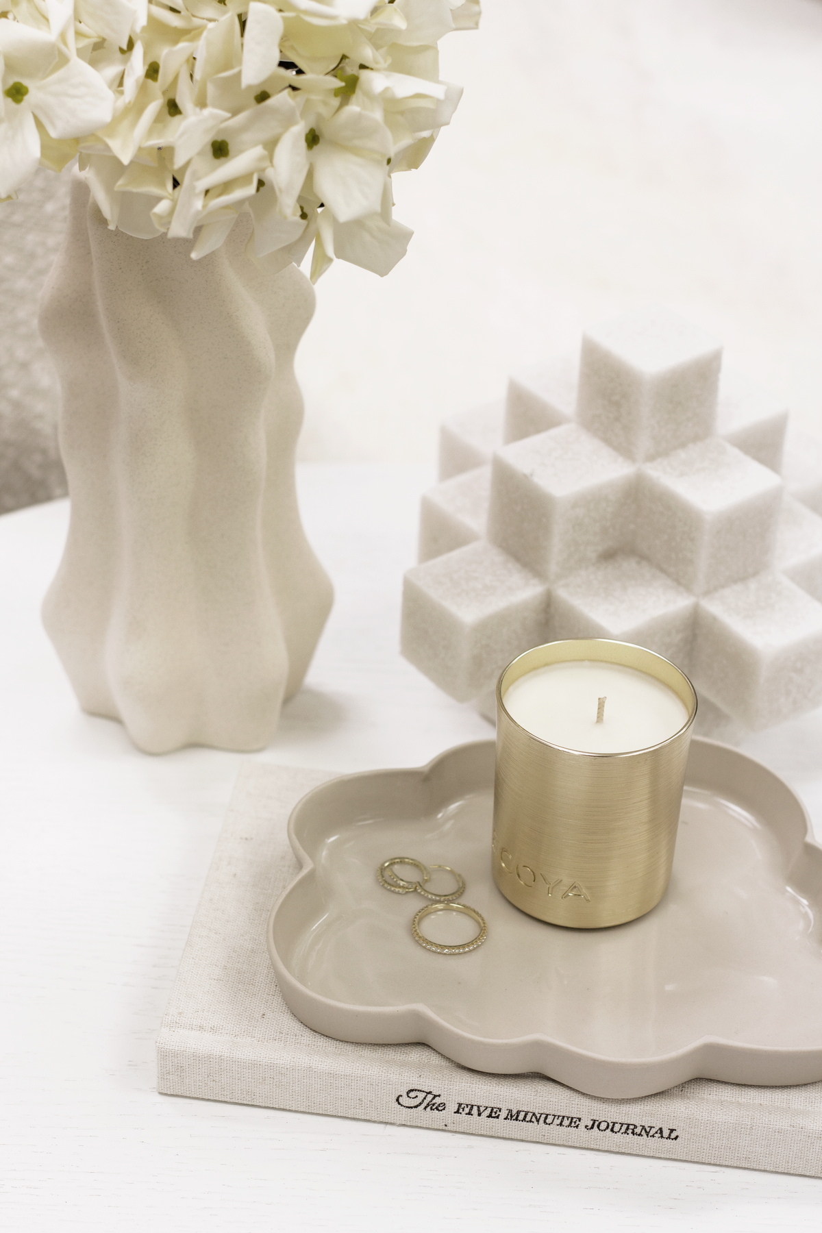 White Cubism sculpture beside a candle on a scalloped tray and a vase of flowers