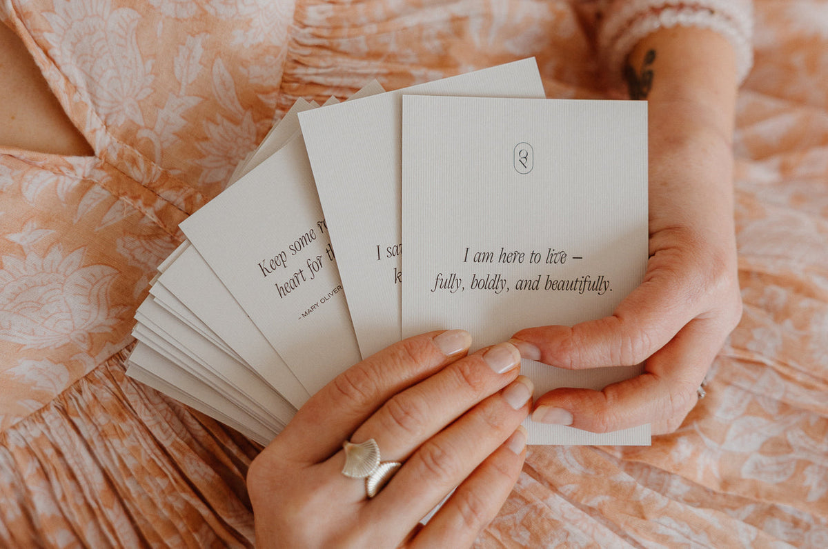 Hands fanning out Art of Living cards over a blush floral dress