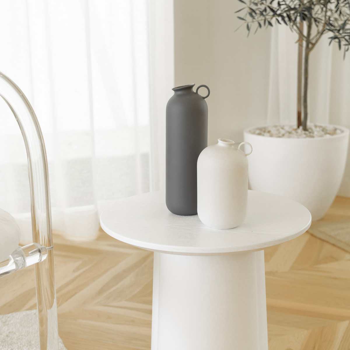Charcoal and white Flugen vases on a round white side table by sheer curtains