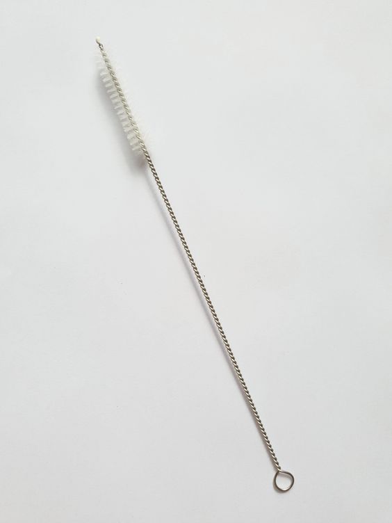 Straw cleaning brush angled across a plain pale surface, bristle head and wire loop in view