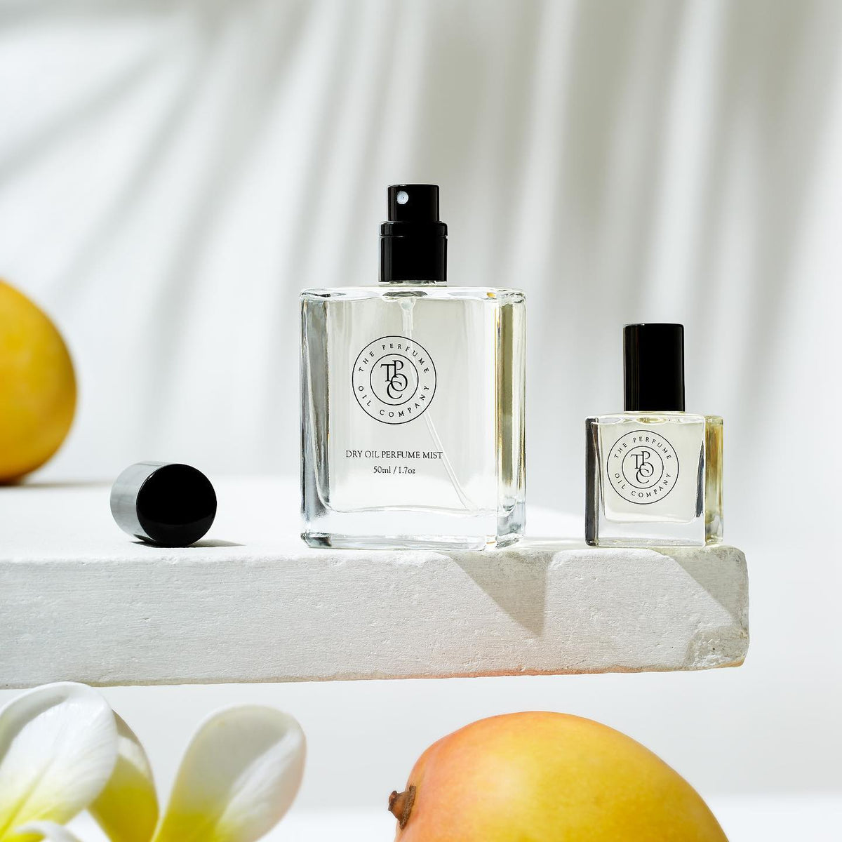 Perfume mist and roll-on bottles on a white plinth with mango and frangipani