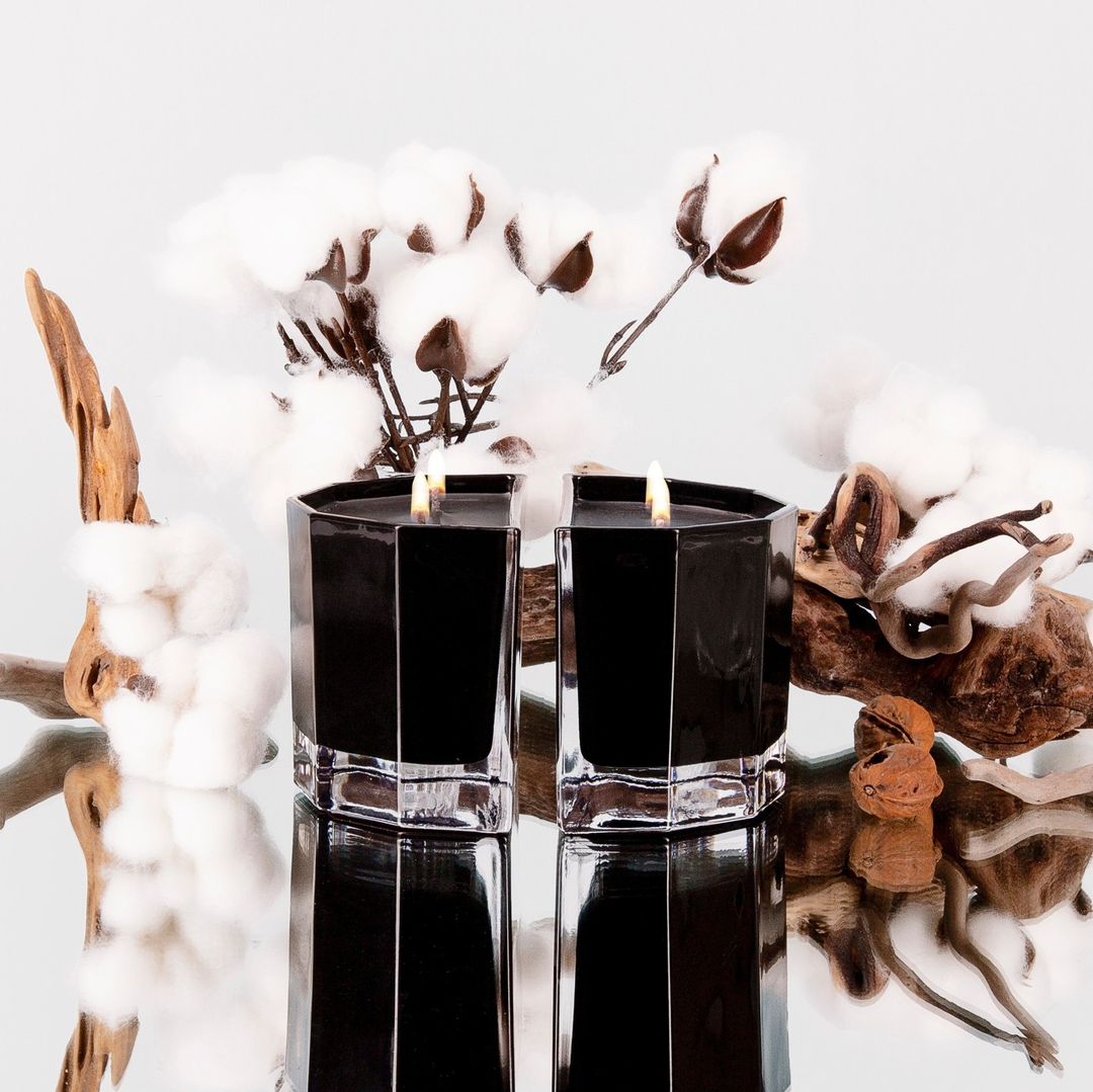 Two lit Blend candles in black glass on a mirrored surface with cotton stems and driftwood