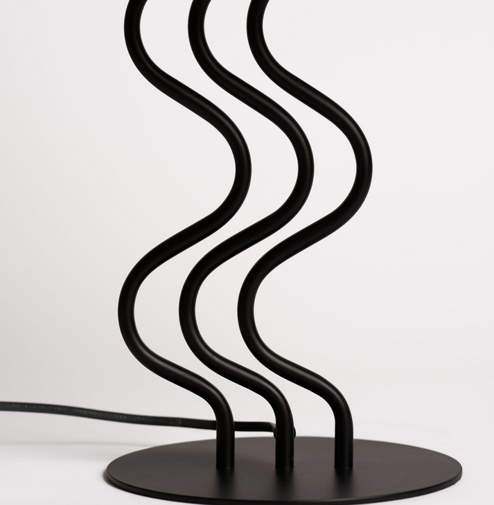 Close-up of the Surge lamp's black ribbon-like steel stem and round base