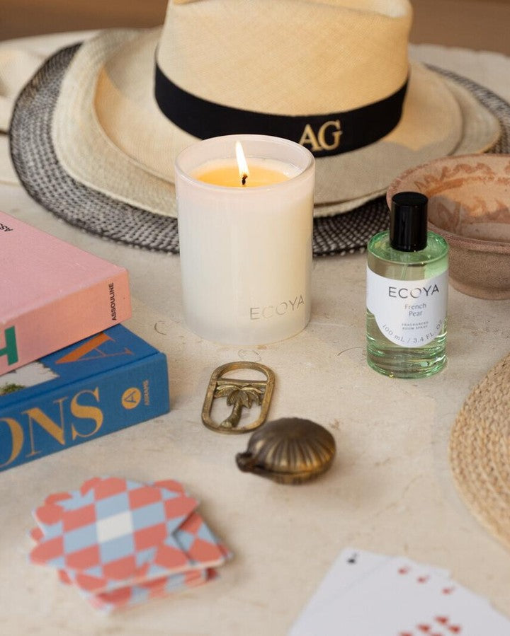 Summer flat lay with a straw hat, lit candle, Ecoya room spray and a pink tray