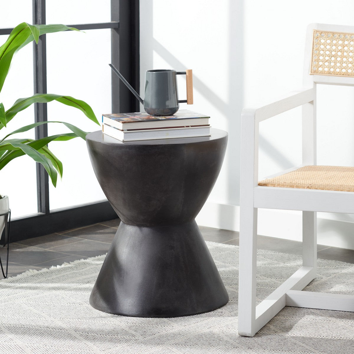 Black Westside accent table beside a cane chair with books and a jug on top