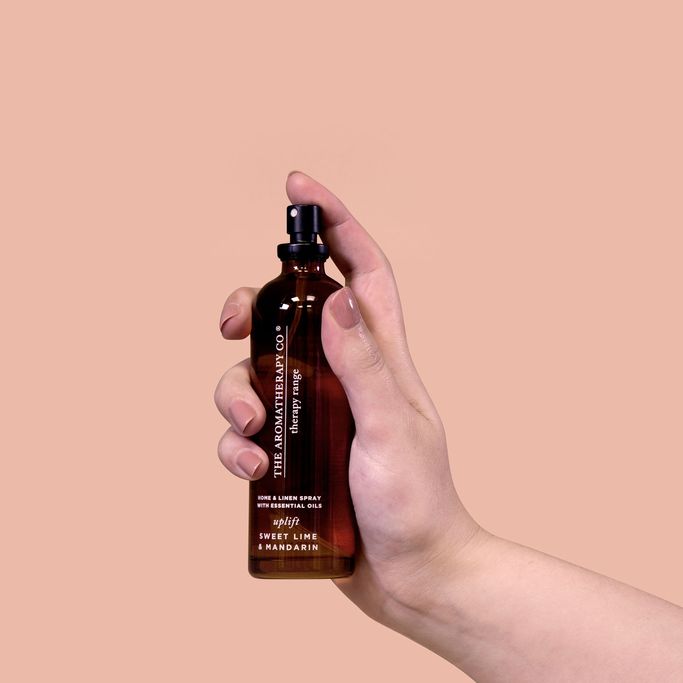 Hand holding the Uplift Sweet Lime & Mandarin room spray against a blush pink background