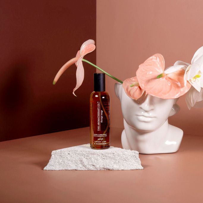 Small amber spray bottle on a stone slab beside a sculptural head vase with pink anthuriums