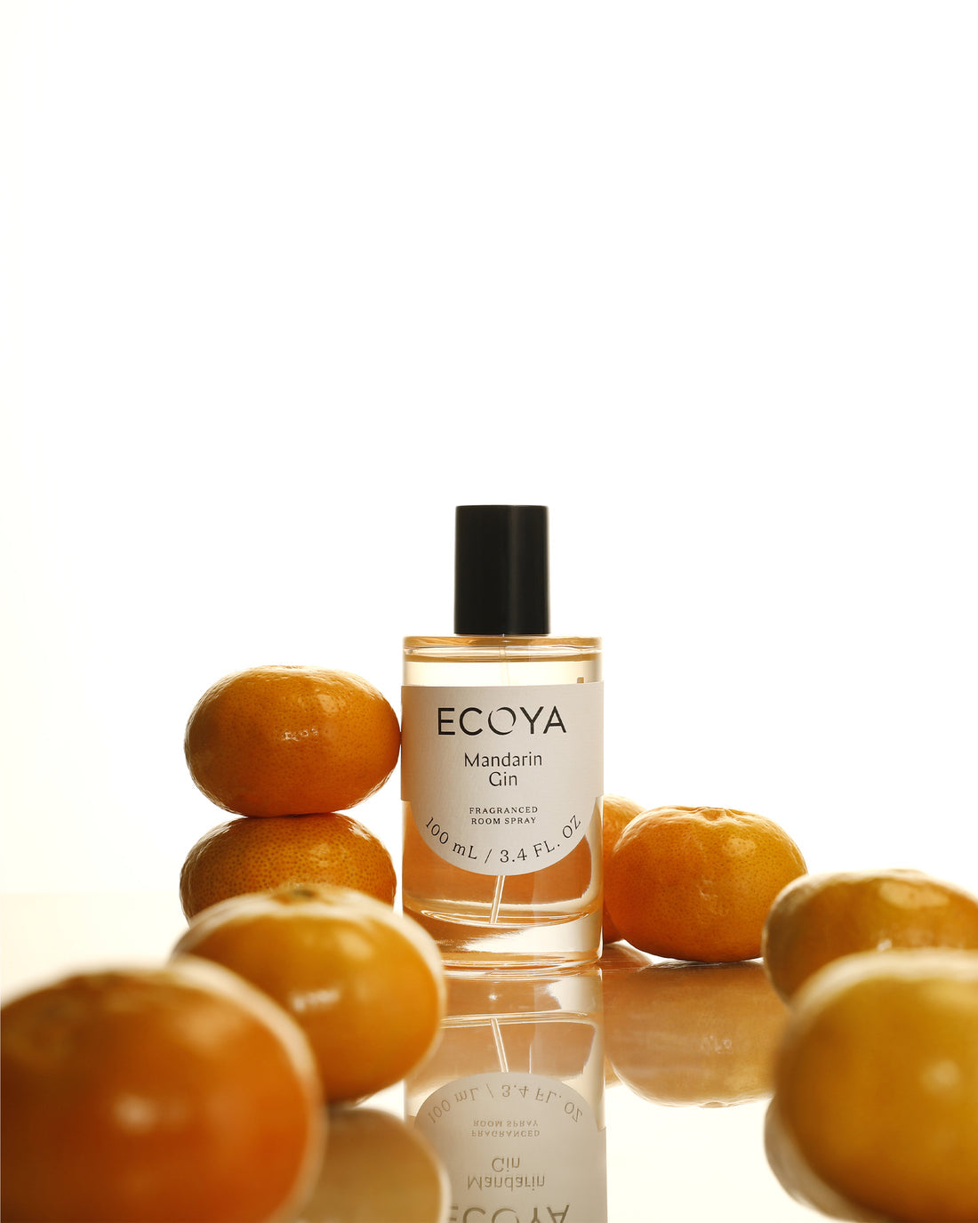 Ecoya Mandarin Gin room spray in orange-tinted glass surrounded by mandarins