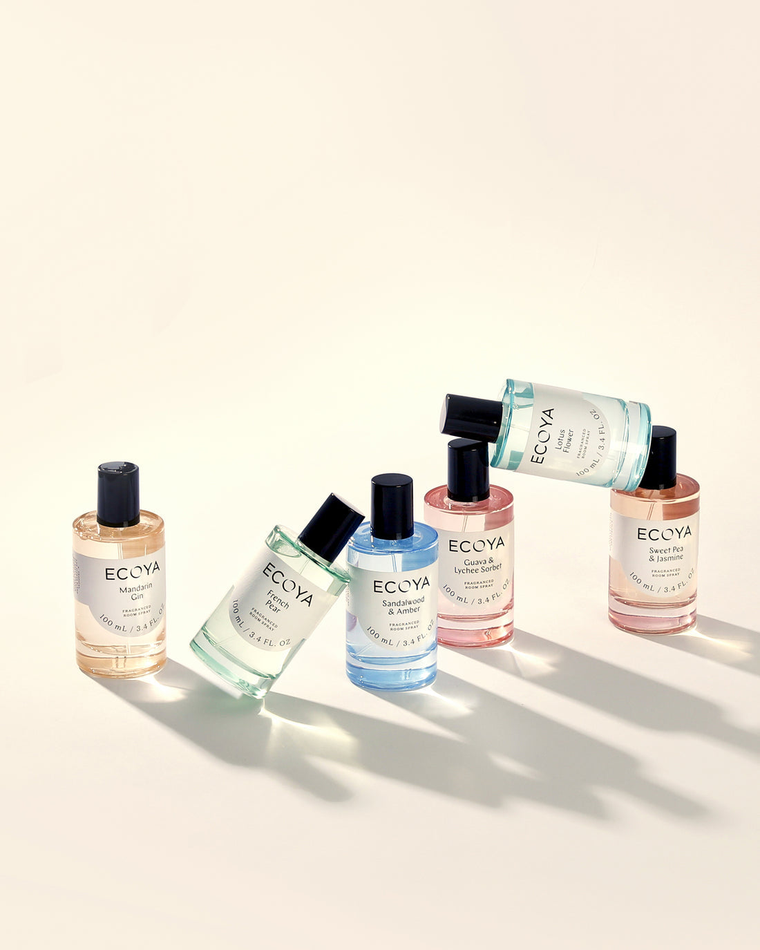 Row of Ecoya room sprays in different coloured glass bottles casting shadows on cream