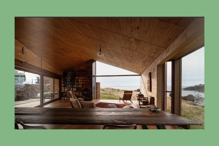 This Building Likes Me spread showing a timber living room with built in bookshelves opening to the coast