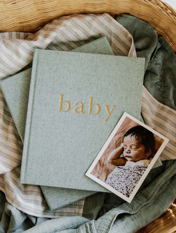A baby book, Write To Me's "Baby - THE FIRST YEAR OF YOU - Boxed Baby Journal," with a photo of a baby in a basket.