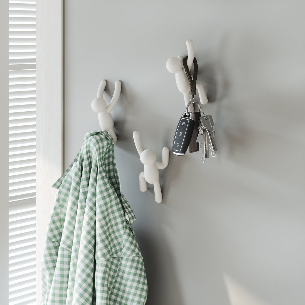 Umbra Buddy hooks in white on a wall, holding a green gingham towel and a set of keys