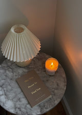 A "This Was Meant To Find You (When You Needed It Most)" book and a candle on a table next to a lamp. (Brand: Thought Catalog)