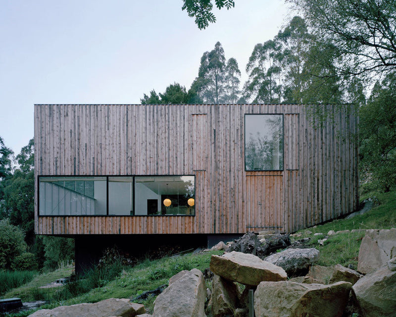 A contemporary wooden house sits on a hillside, capturing the essence of modern design and lifestyle showcased in the book "Rock the Shack" by Books.