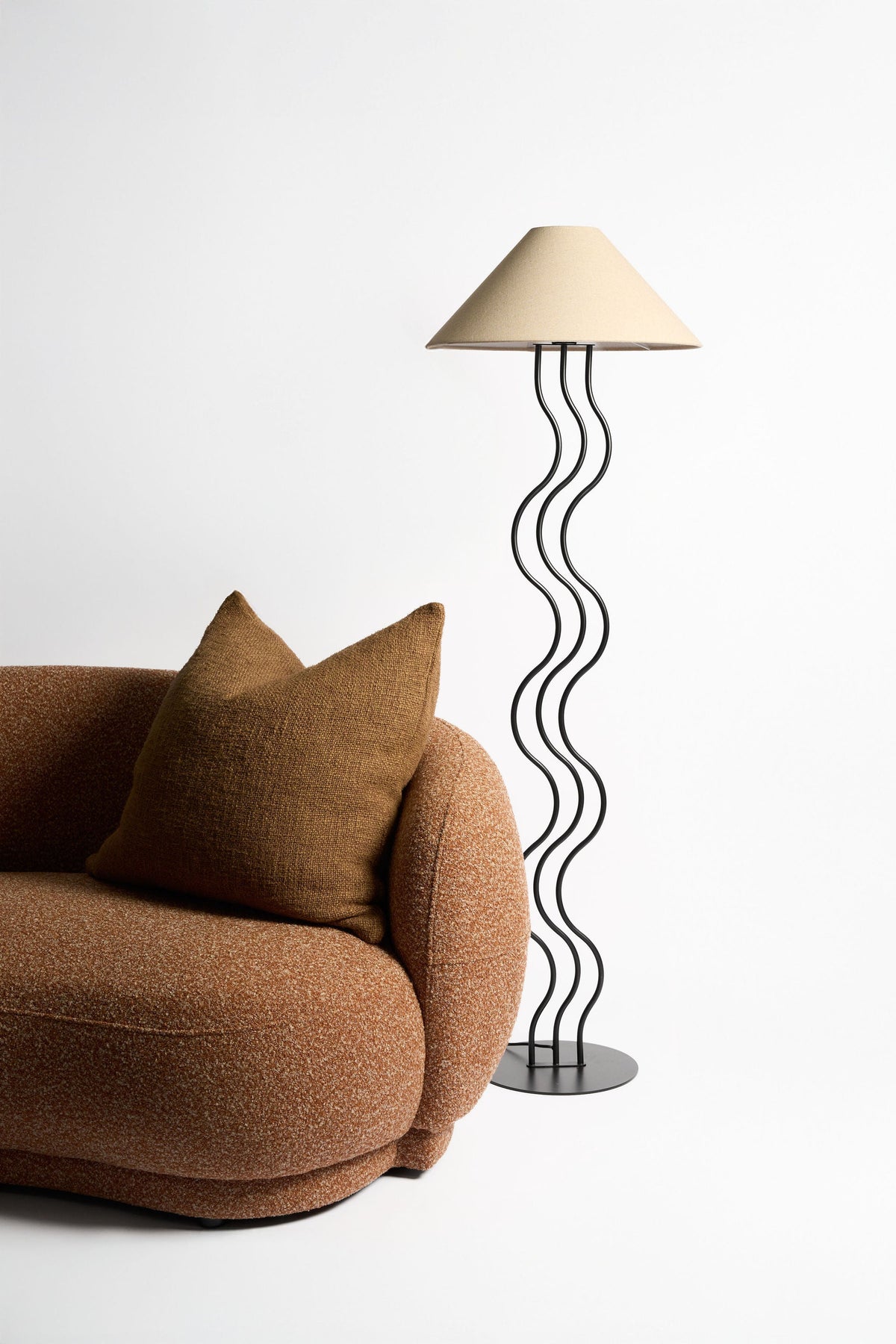 Surge floor lamp beside a curved brown boucle armchair